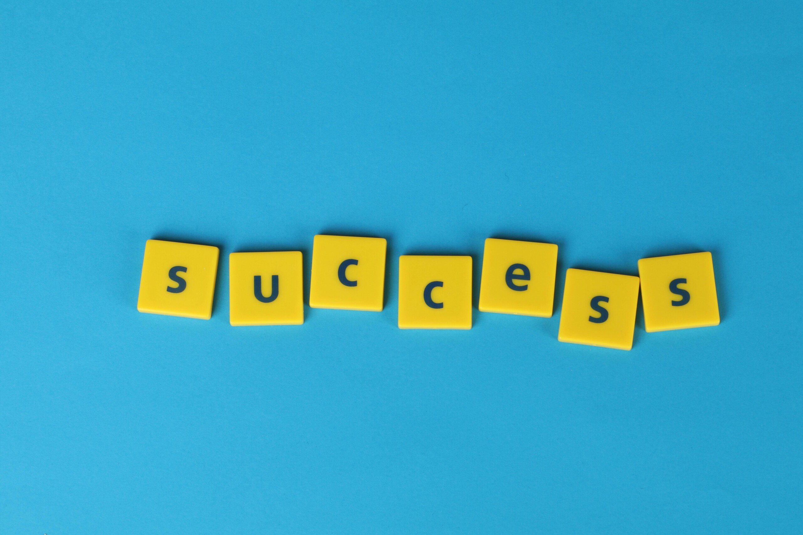 our-services-02 Yellow letter tiles spell the word success on a vibrant blue backdrop, symbolizing achievement.