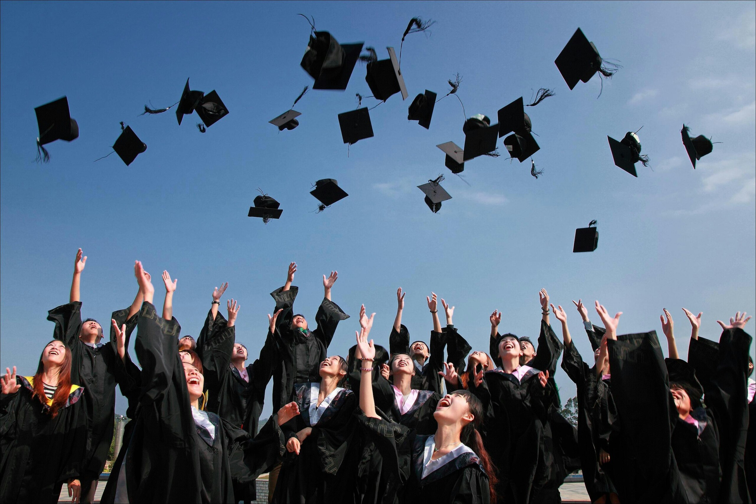 our-services-03 Group of graduates celebrating by throwing caps in the air during a sunny day.